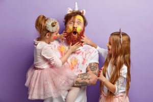 Surprised Dad and Two Girls Play Together at Home, Paint Faces with Watercolours, Have Fun, Show Hands Painted in Bright Colours, Isolated over Purple Background. Family Portrait. Fatherhood