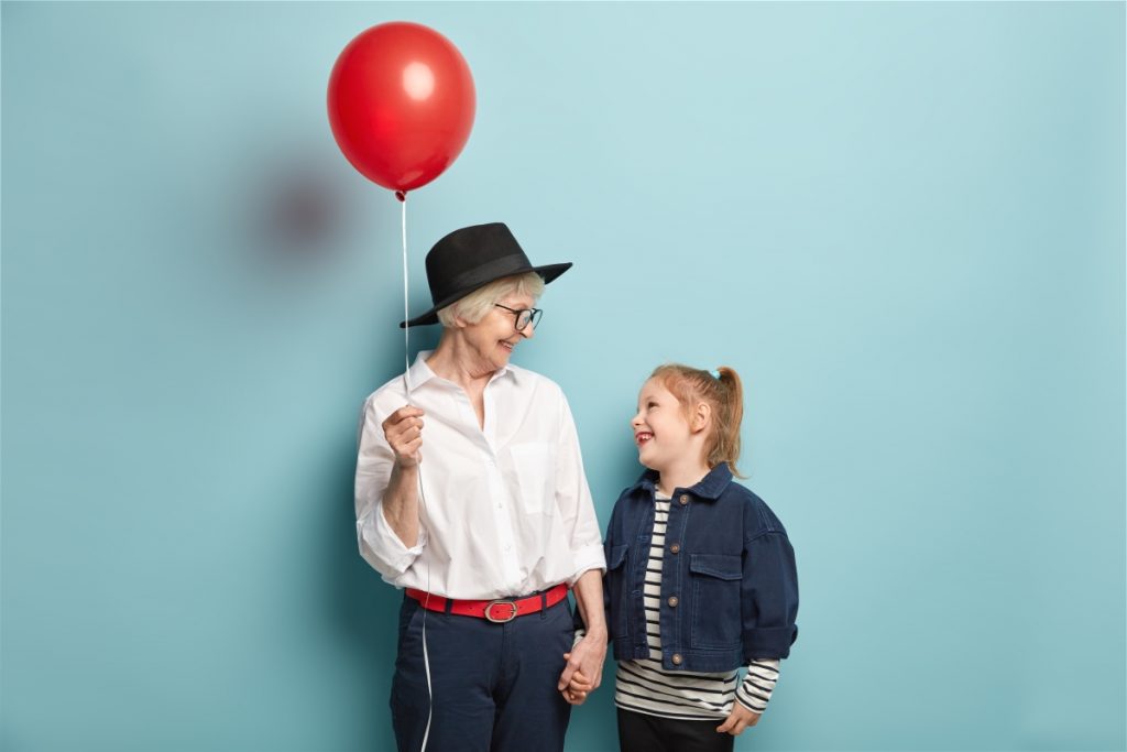 studio-shot-of-happy-small-child-holds-hand-of-grandmother-with-balloon-look-at-each-other-spend-free-time