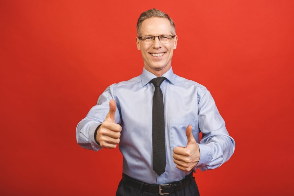well-done-close-up-portrait-of-delightful-confident-cool-glad-pleased-cheerful-excited-aged-senior-business-man-demonstrating-thumb-up-smile-isolated-on-red-wall