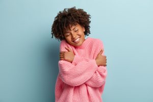 mixed race woman in pink jumper smiles and hugs herself