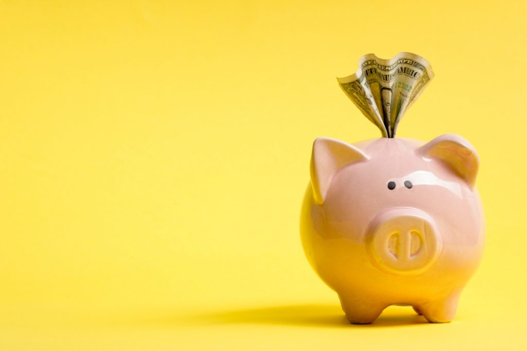 pink piggy bank with money emerging on yellow background