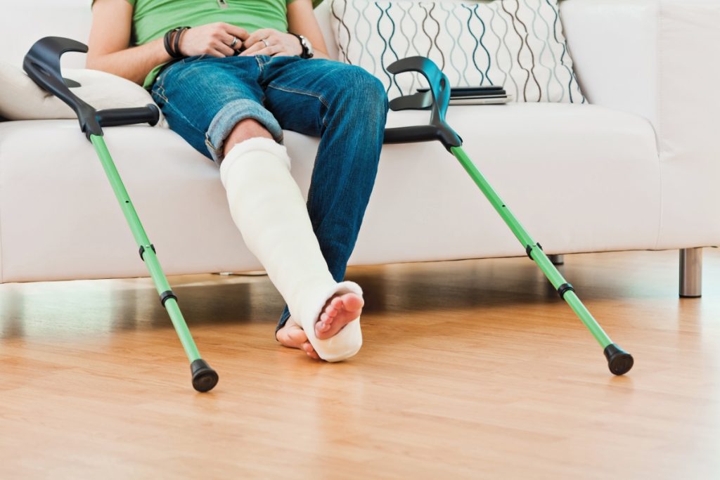 person wearing jeans sits on a sofa with a broken leg . crutches are either side of them