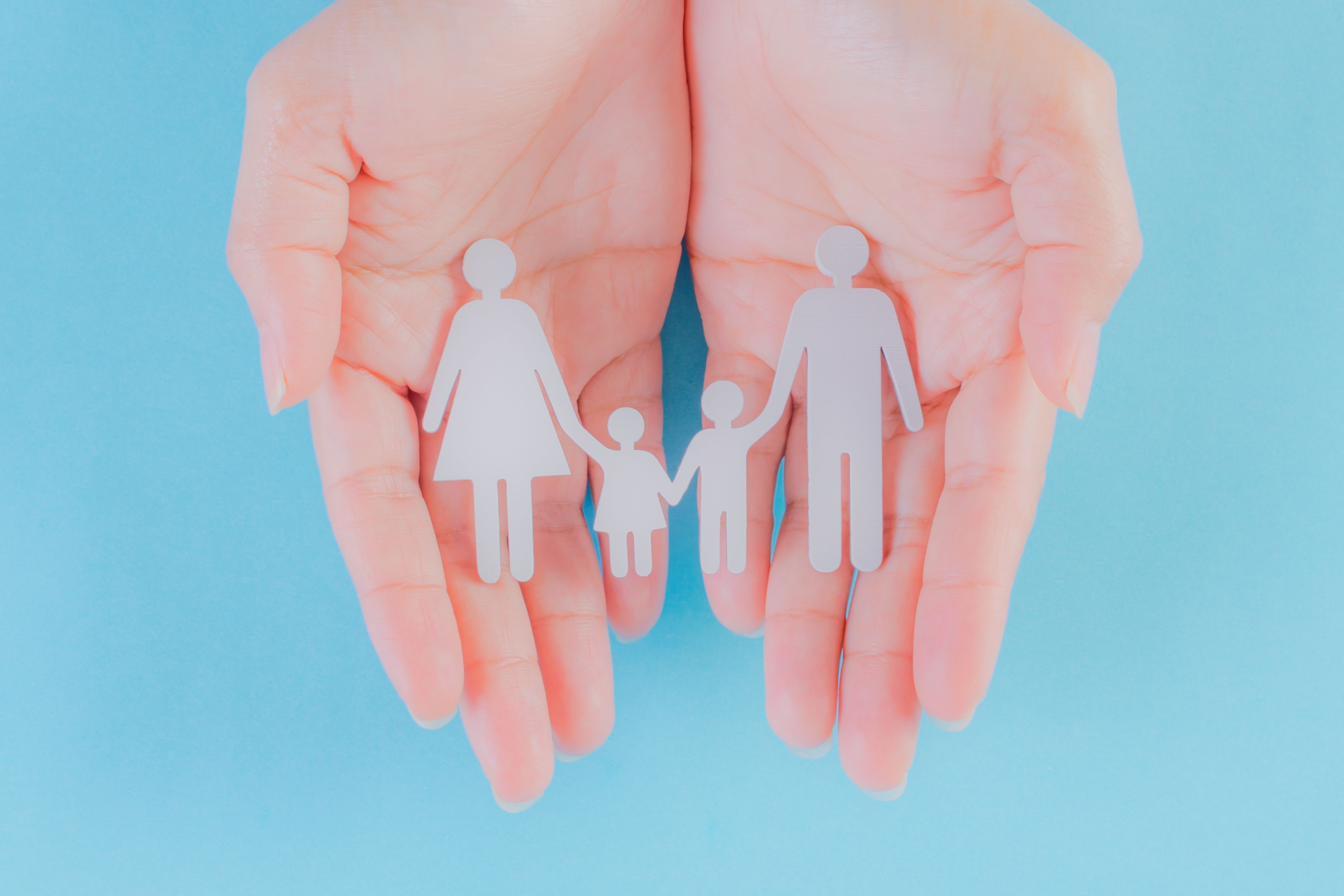 pair of hands on a light blue background cradling a small paper put out of a family