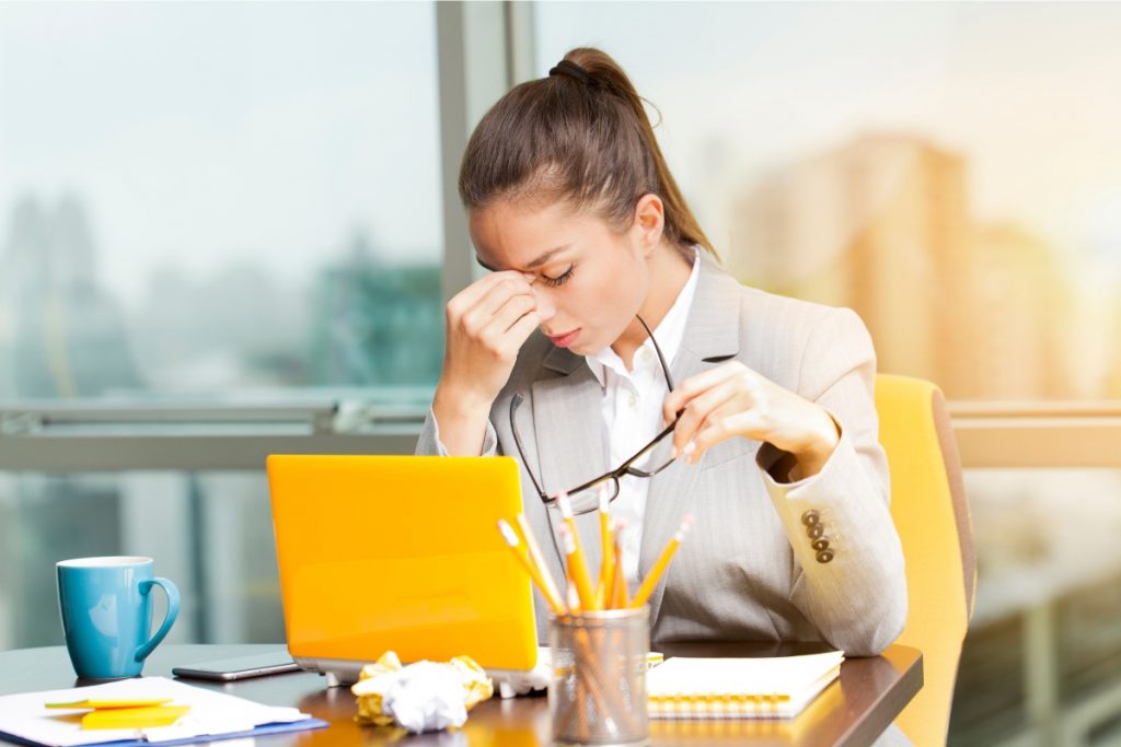 woman sits at yellow laptop looking stressed